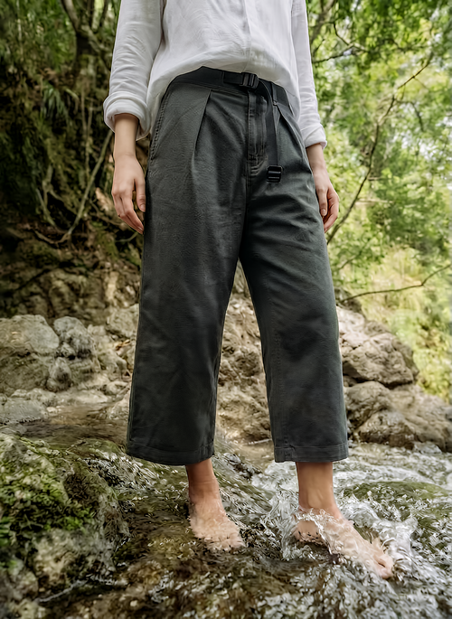 Person wearing dark pants standing in a natural setting with rocks and greenery.
